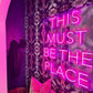 Neon sign reading 'THIS MUST BE THE PLACE' in a room with patterned wall and pink accents.