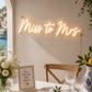 Neon sign reading 'Miss to Mrs' above a table setting with flowers and glasses.