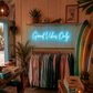 Neon sign reading 'Good Vibes Only' in a clothing store with surfboards and plants.