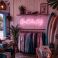 Neon sign reading 'Good Vibes Only' in a clothing store with surfboards and plants.