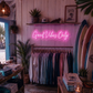 Neon sign reading 'Good Vibes Only' in a store with clothing racks and surfboards.