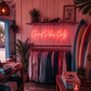 Neon sign 'Good Vibes Only' in a store with clothing racks and surfboards.