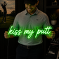 Man holding a neon sign with 'kiss my putt' in a golf-themed room.