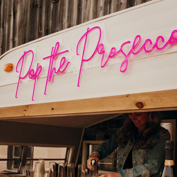 Bar with 'Pop the Prosecco' neon sign and a person behind the bar.