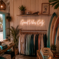 Neon sign 'Good Vibes Only' in a store with clothing racks and surfboards.