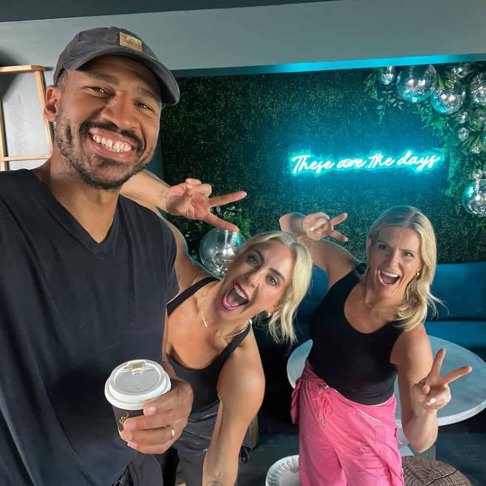 Three people posing together with a neon sign in the background