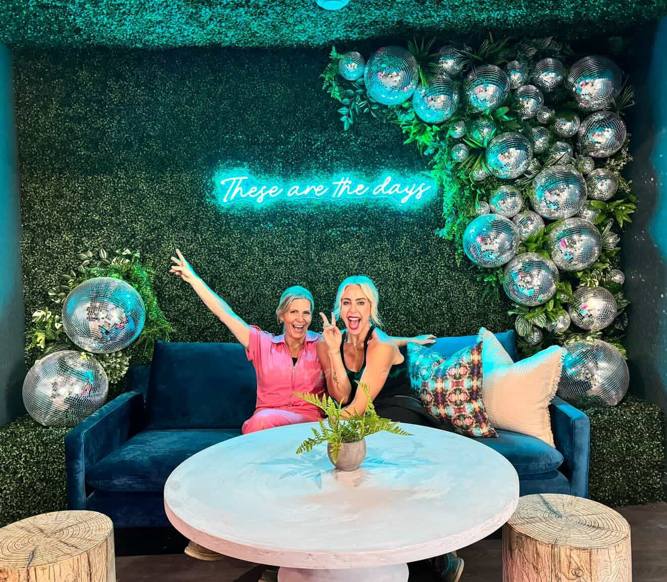 Two women sitting on a couch in a decorated room with disco balls and a neon sign.