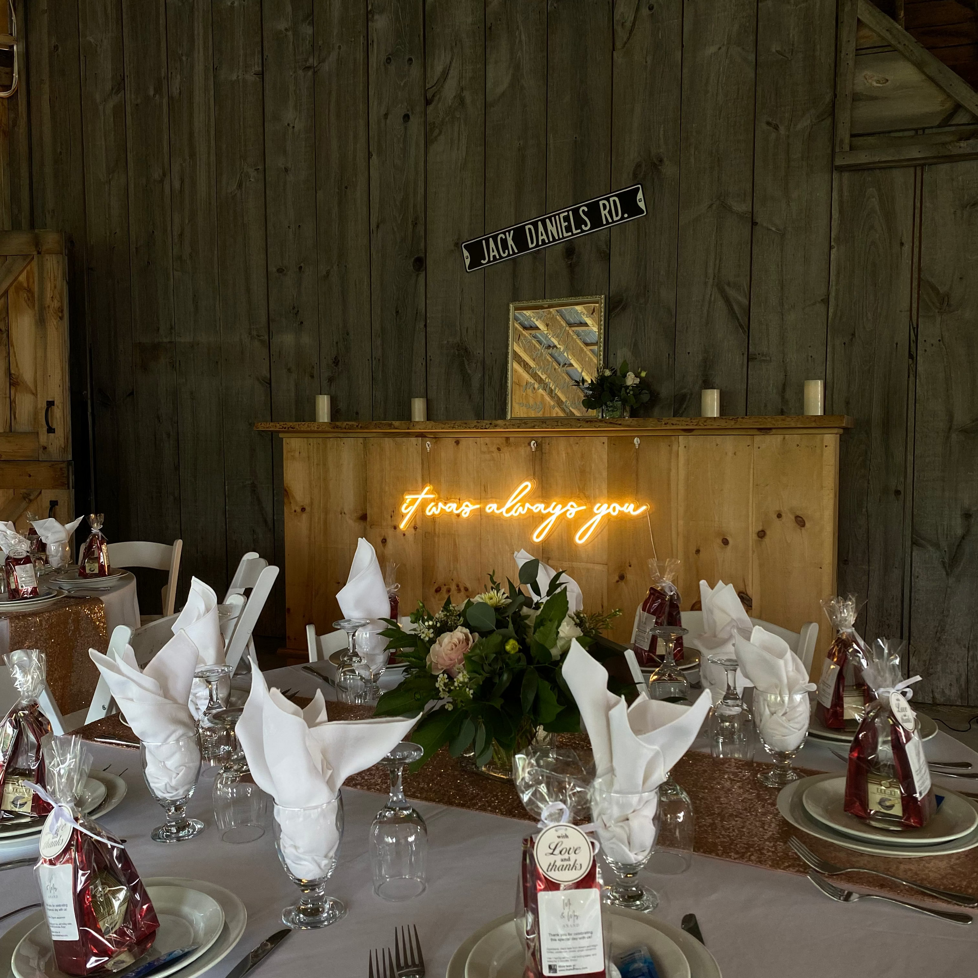 Decorated table setting with floral centerpieces and neon sign in a rustic wooden room.